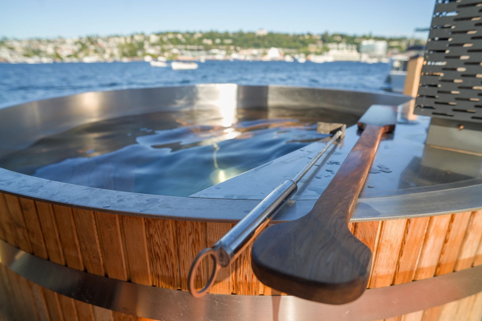 Close-up of the wood-fired hot tub rim with a wooden ladle, Lake Union behind it