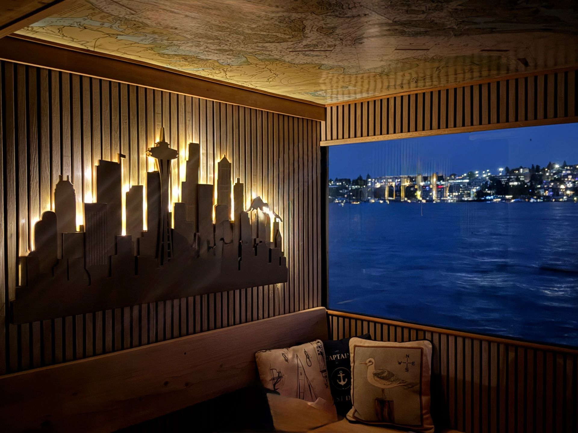 Warm wood lounge aboard Banya Boat at night with illuminated Seattle skyline artwork and lake views