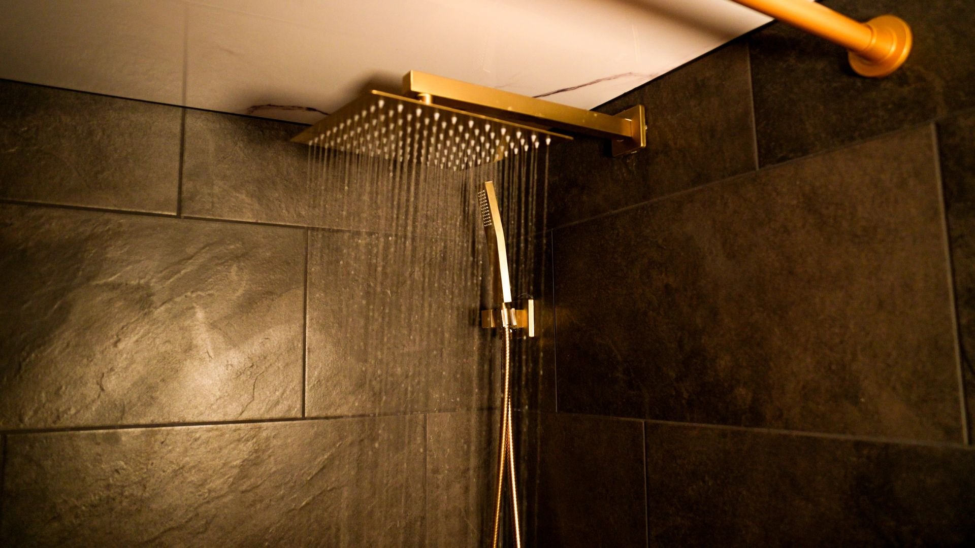 Brass rain shower running in the dark slate-tiled shower room aboard Banya Boat